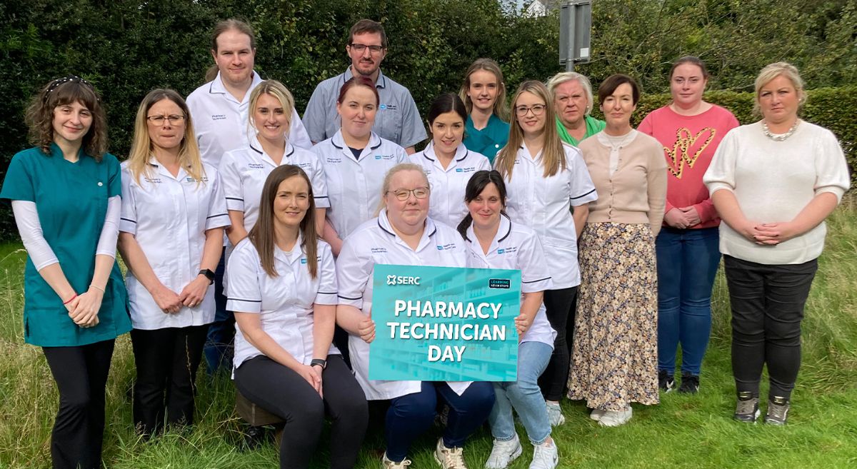 A goup of 16 students, wearing medical tunics with SERC lecturers in the Wellbeing Garden at Holywood Campus